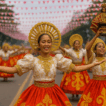 Street dancers in vibrant gold and red Sinulog costumes perform along a decorated road in Cebu City, with one dancer holding a Santo Niño statue amid festive banners and cheering crowds.