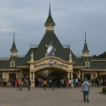 Photorealistic view of Enchanted Kingdom’s main entrance in Santa Rosa, Laguna, showing the Victorian-style gateway, green turrets, and crowds of visitors.