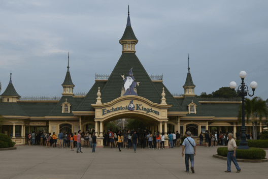 Photorealistic view of Enchanted Kingdom’s main entrance in Santa Rosa, Laguna, showing the Victorian-style gateway, green turrets, and crowds of visitors.